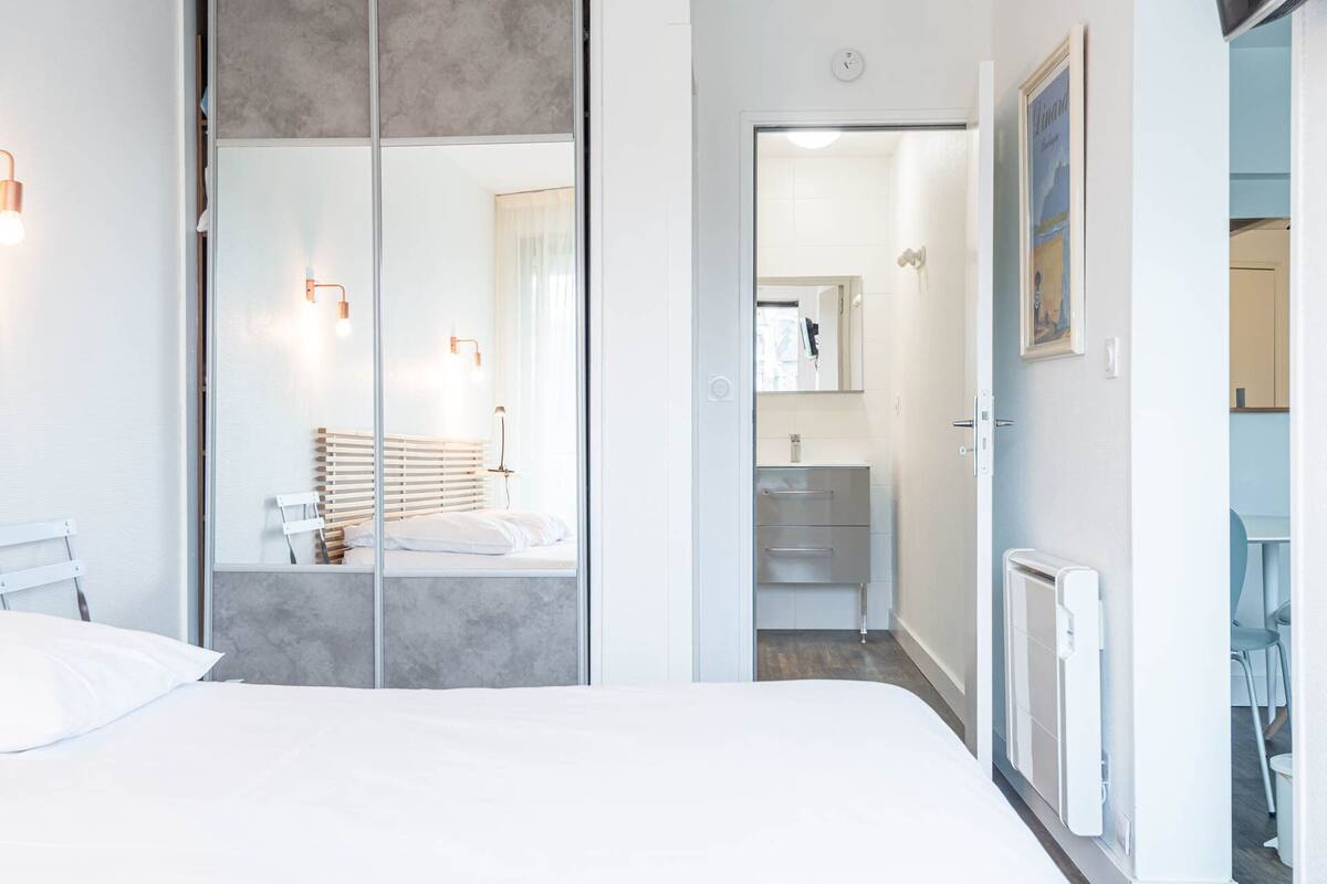 Un dormitorio moderno con una cama grande, un armario con espejo y un baño visible a través de una puerta abierta.
