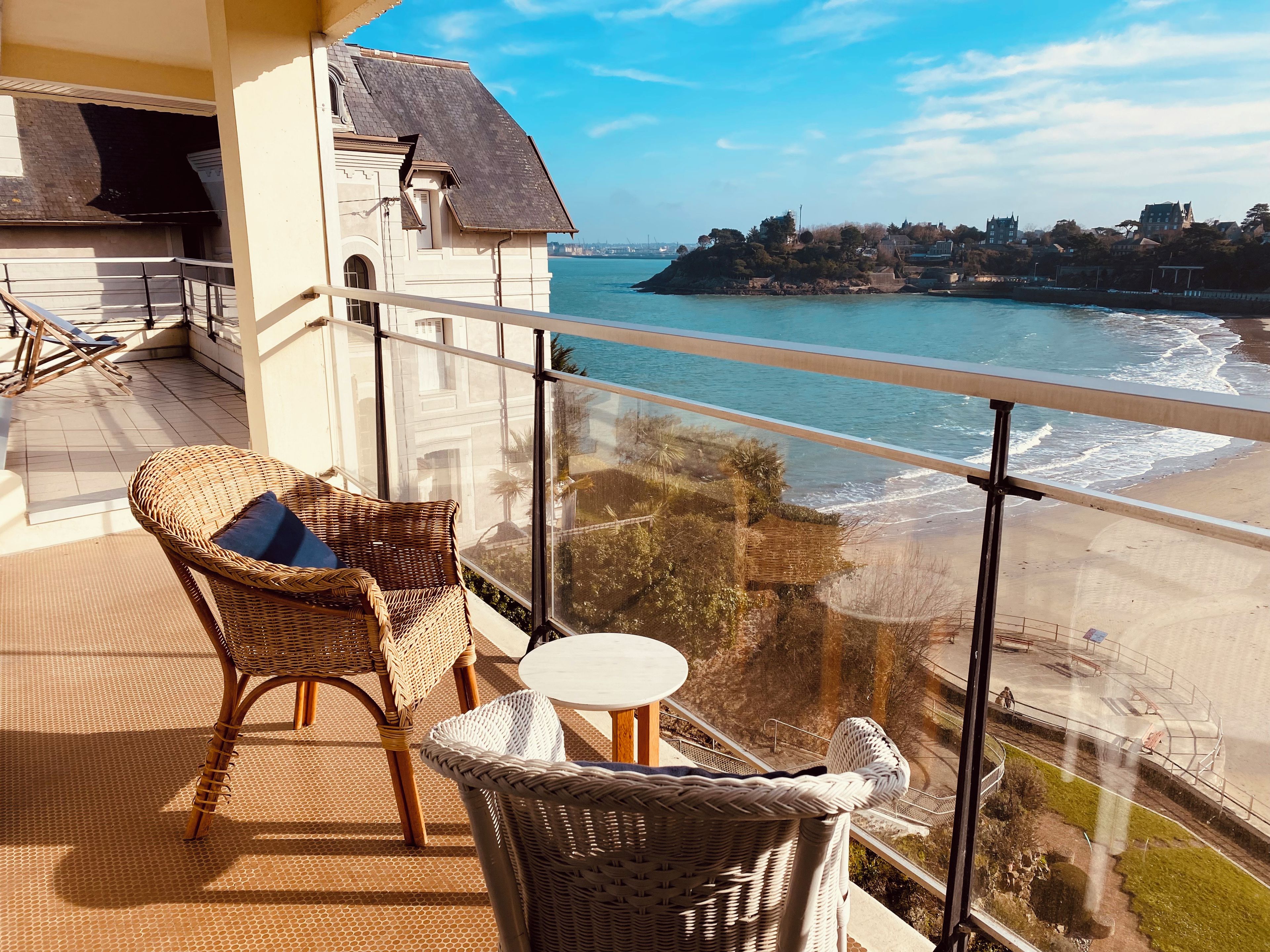 Ein Balkon mit Korbmöbeln und Blick aufs Meer.