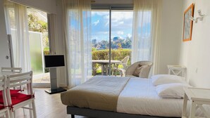 A bedroom with a bed, a chair, a TV, and a view of greenery outside. - Résidence Le Crystal (Dinard)