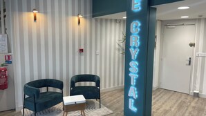 A reception area with a striped wall, two dark chairs, a small table, and a neon sign reading 'THE CRYSTAL.' - Résidence Le Crystal (Dinard)