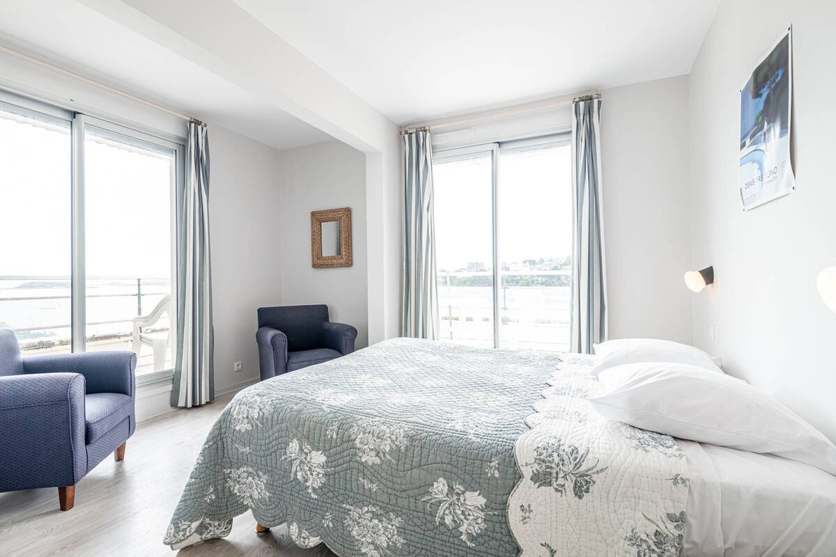 Un dormitorio con una cama grande, una silla y vista al mar a través de amplios ventanales.