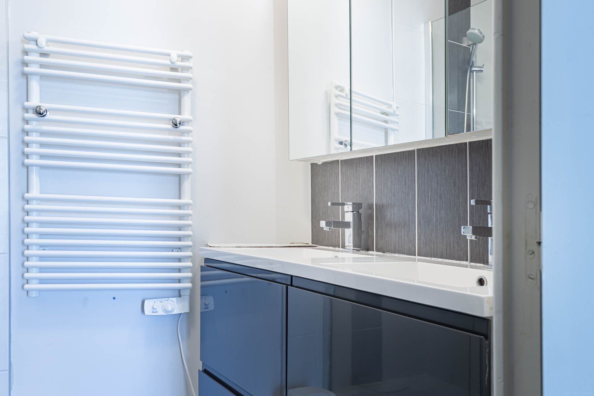 A modern bathroom with a white towel rack, a glass shower enclosure, and a sink with a mirror above it.