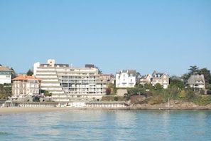 Een hotel aan de kust met meerdere verdiepingen, een strand op de voorgrond en een mix van woon- en bedrijfsgebouwen op de achtergrond.