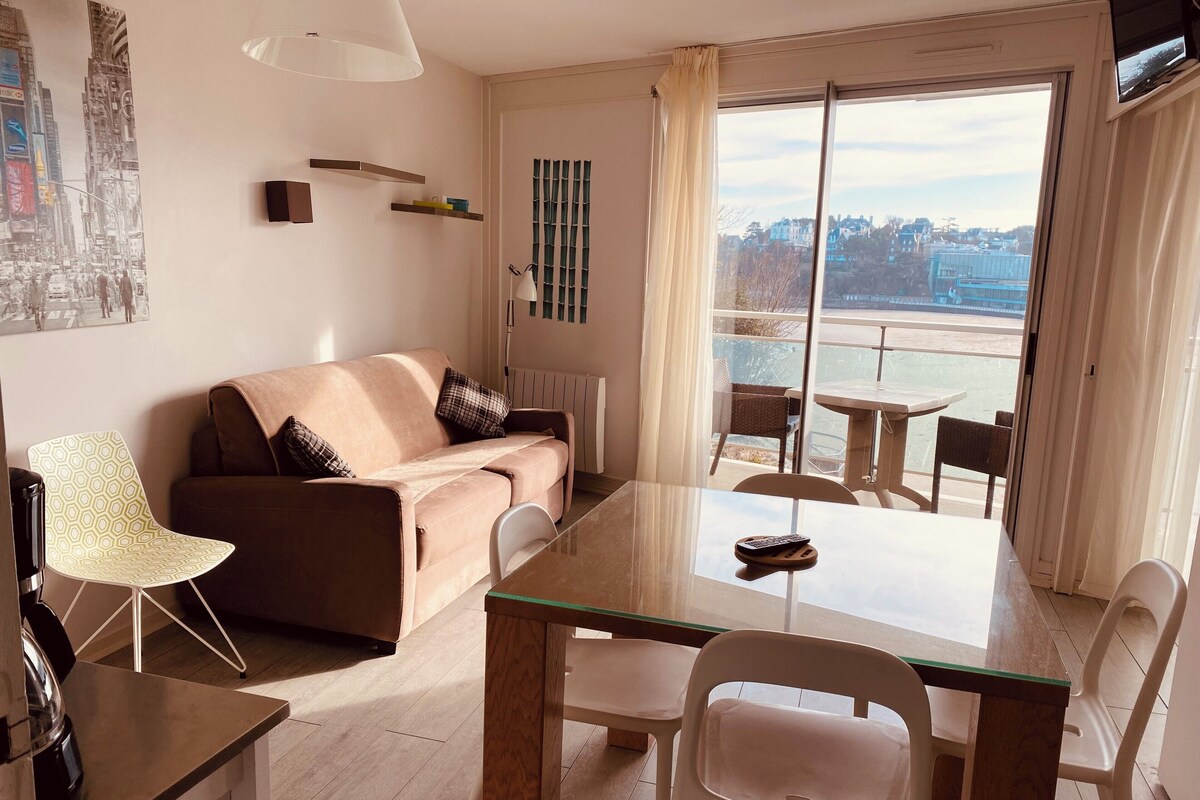 Een moderne woonkamer met een bank, een eettafel, stoelen, een radiator, een televisie en een stadszicht door het raam.