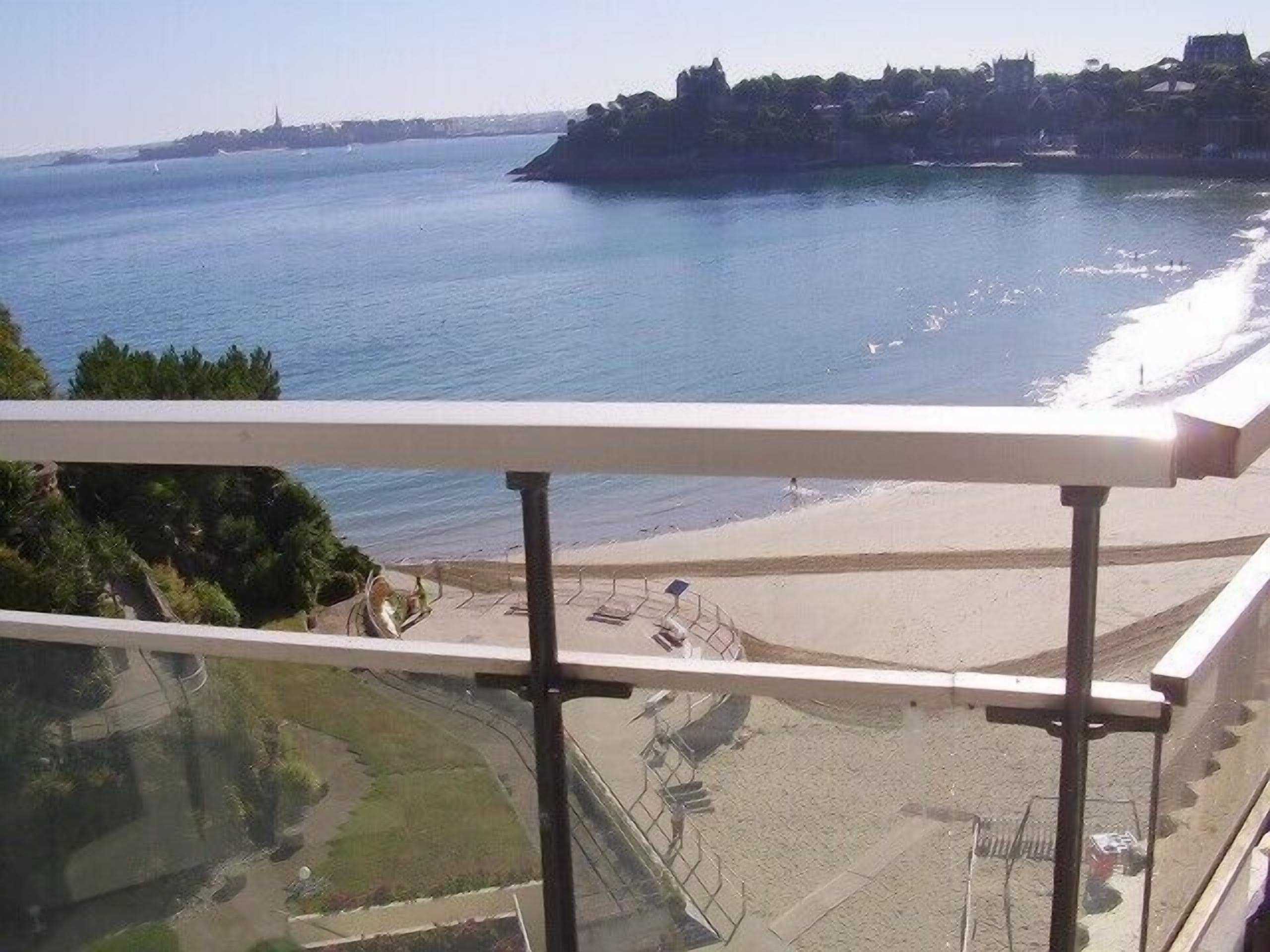 A coastal view from a balcony with a railing, overlooking a beach and the sea.