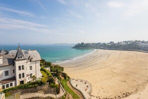 A coastal view with a sandy beach, a promenade with benches, and a historic building with a tower. - Résidence Le Crystal (Dinard)