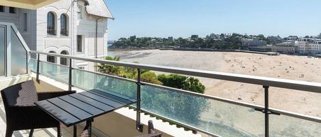 A balcony with a view of a beach and a building with arched windows.