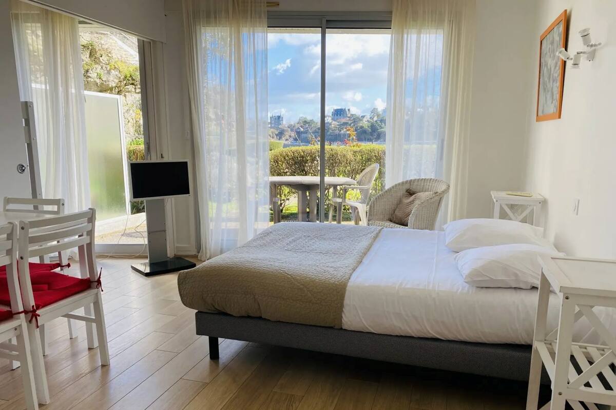 Un dormitorio con cama, una silla, televisor y balcón con vistas.