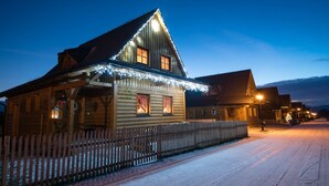 Uma cabana de tronco de madeira com telhado inclinado, cerca de madeira e chão coberto de neve.