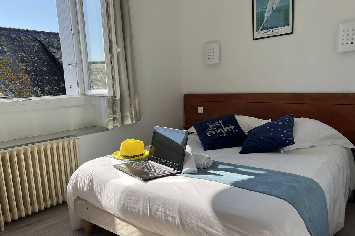 A neatly made bed with a laptop, a yellow hat, and decorative pillows.