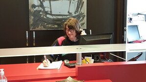 Un mostrador de recepción con una persona escribiendo, un cuadro en la pared y una ventana con vistas al exterior.