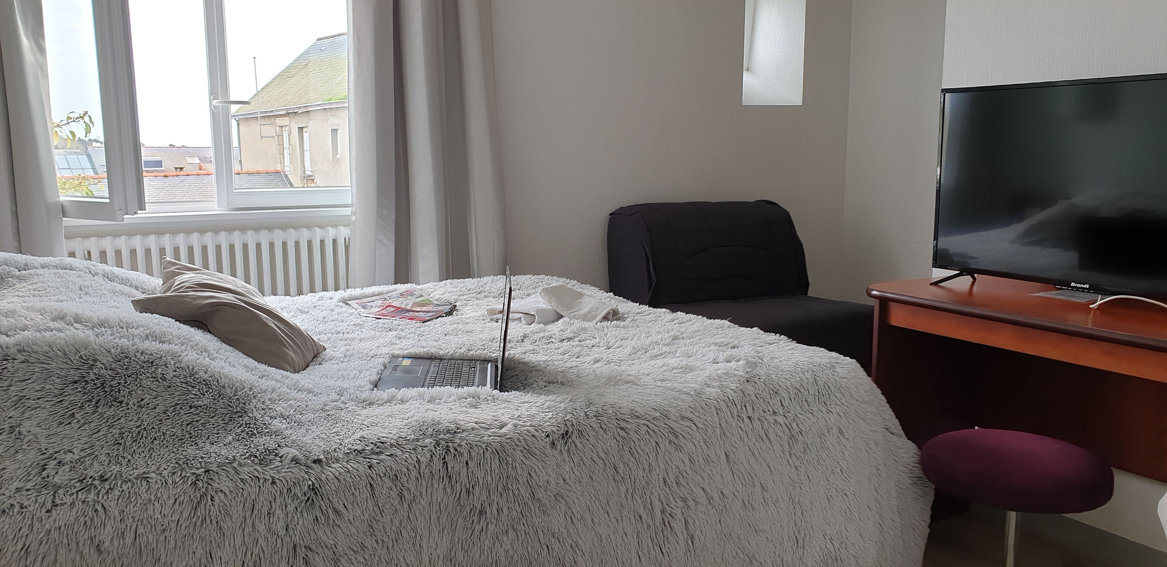 Una habitación de hotel con cama, escritorio con televisor, silla y ventana con cortinas.