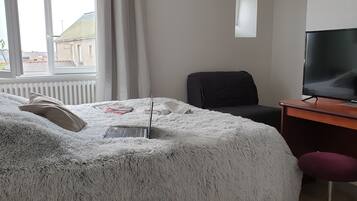 Una habitación de hotel con cama, escritorio con televisor, silla y ventana con cortinas.