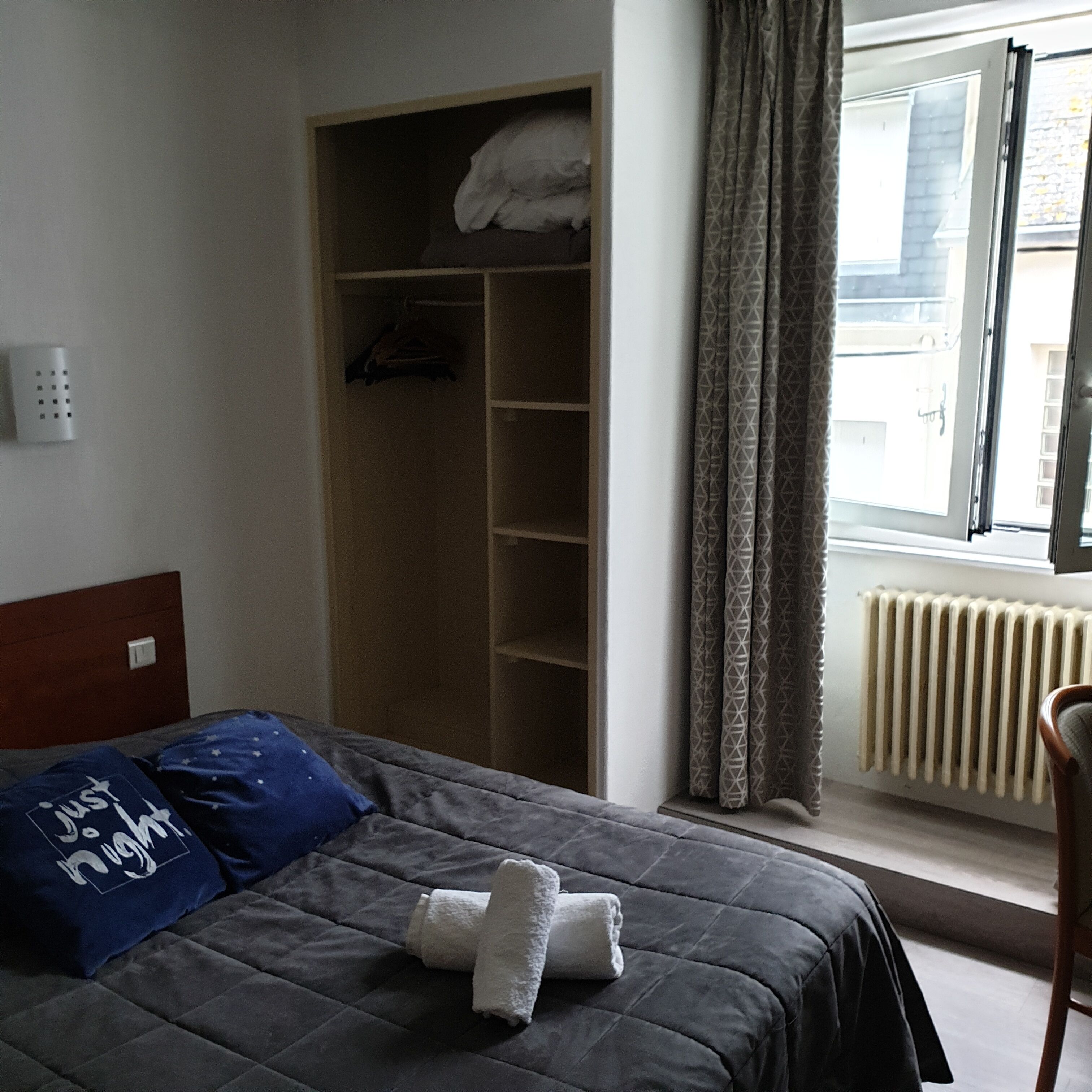 Een slaapkamer met een bed, een kledingkast, een radiator en een raam met gordijnen.