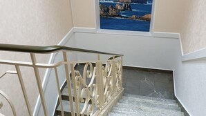 Una escalera con barandilla metálica y vista a la costa rocosa a través de una ventana.