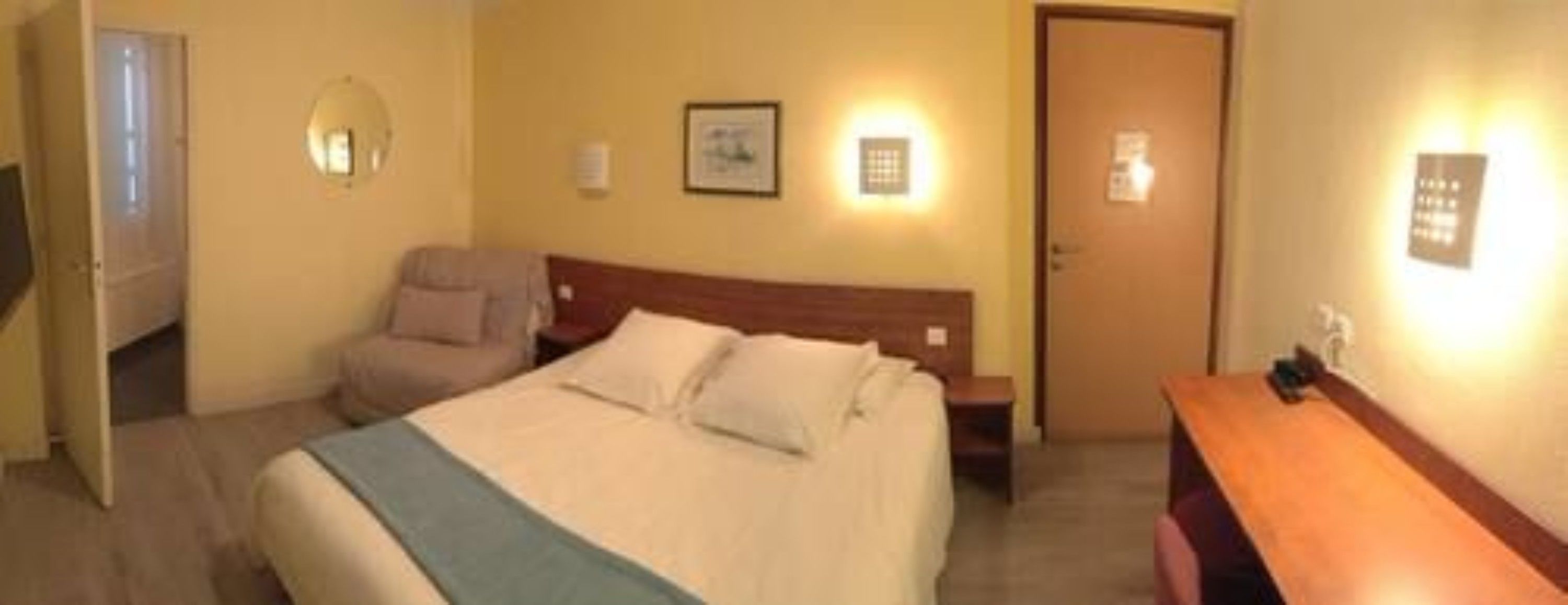 Ett hotellrum med en säng, en stol, ett skrivbord och en dörr.