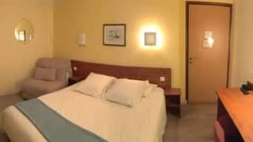 Quarto de hotel com cama, cadeira, escrivaninha e porta.