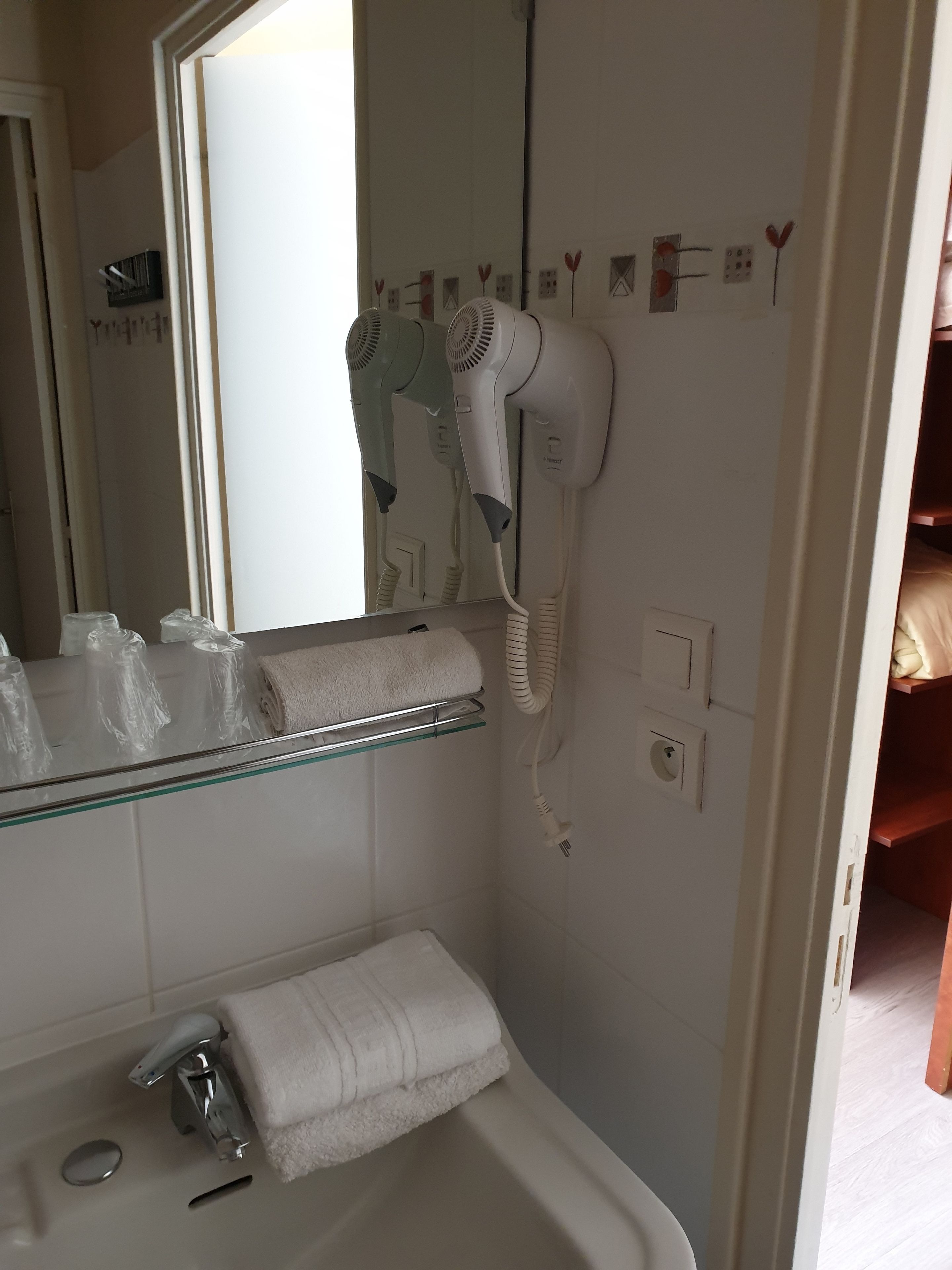 A bathroom with a white sink, a glass shelf with toiletries, a towel rack, and a hairdryer mounted on the wall.