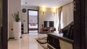 Una habitación de hotel moderna con una televisión de pantalla plana, un sofá, una mesa de centro, una planta grande en maceta y una cama con vista al pasillo.