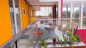 Un balcón con mobiliario de mimbre, baranda de cristal y plantas en macetas.