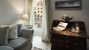 Een kamer met een grijze bank, een houten dressoir met een fotolijst, een lamp en een uitzicht op een stadsbeeld door een raam.
