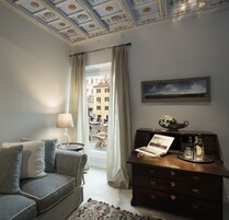 A room with a grey sofa, a wooden dresser with a picture frame, a lamp, and a view of a cityscape through a window.