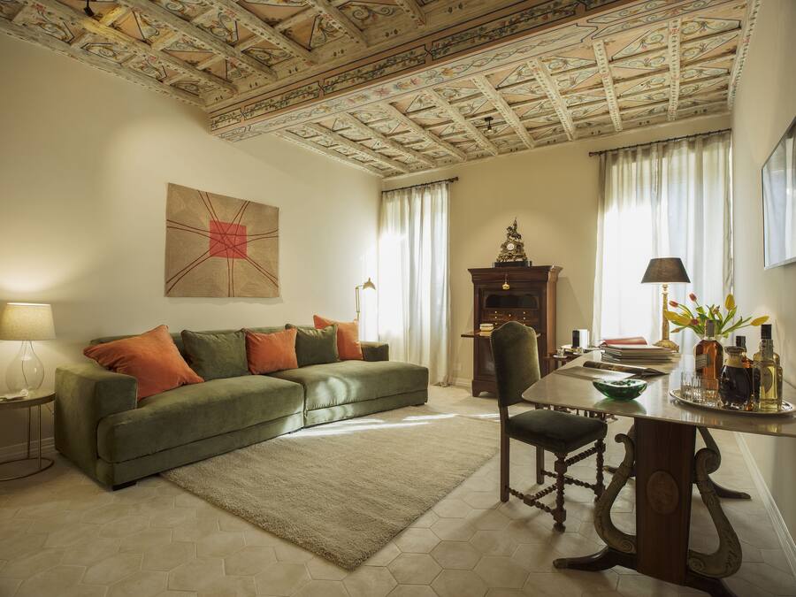 Uma sala de estar com sofá verde, mesa de centro de madeira, lareira e teto com detalhes elaborados.