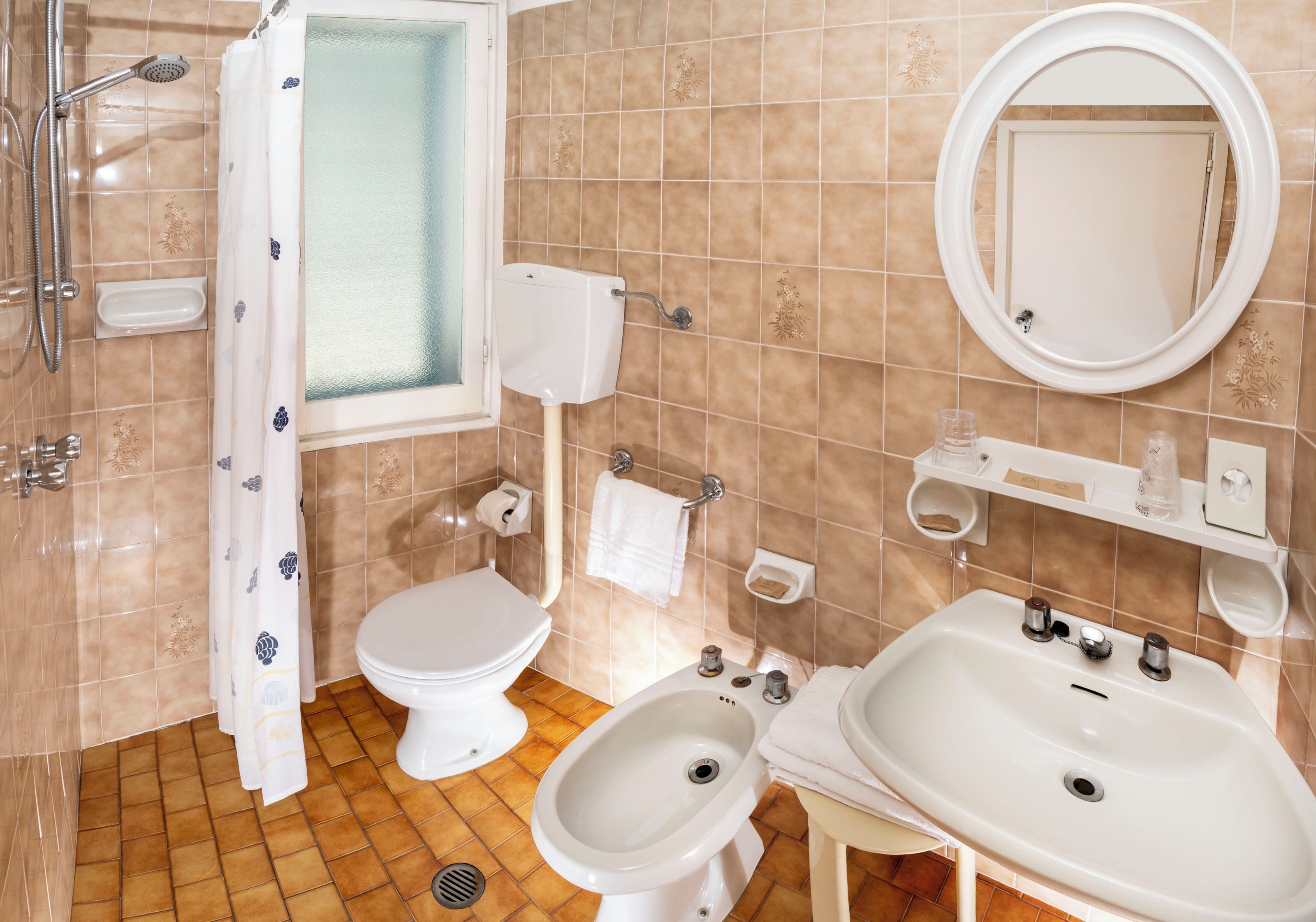 Un baño con inodoro, bidé, lavamanos, espejo y ducha.