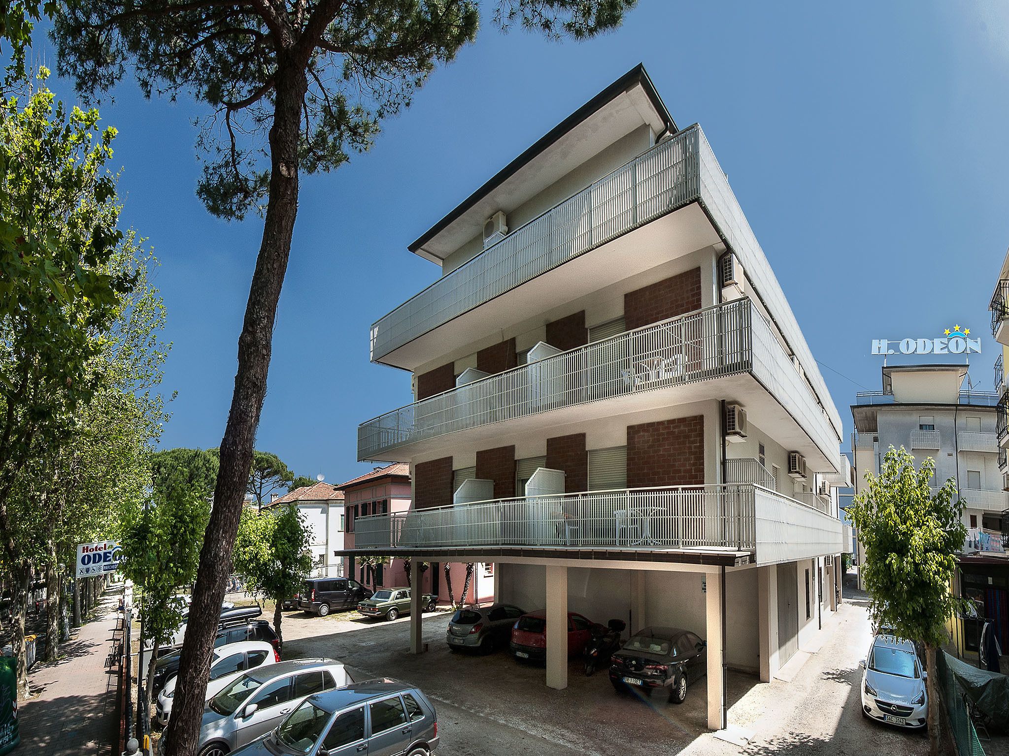 A multi-story hotel with balconies, a parking area, and a clear blue sky.