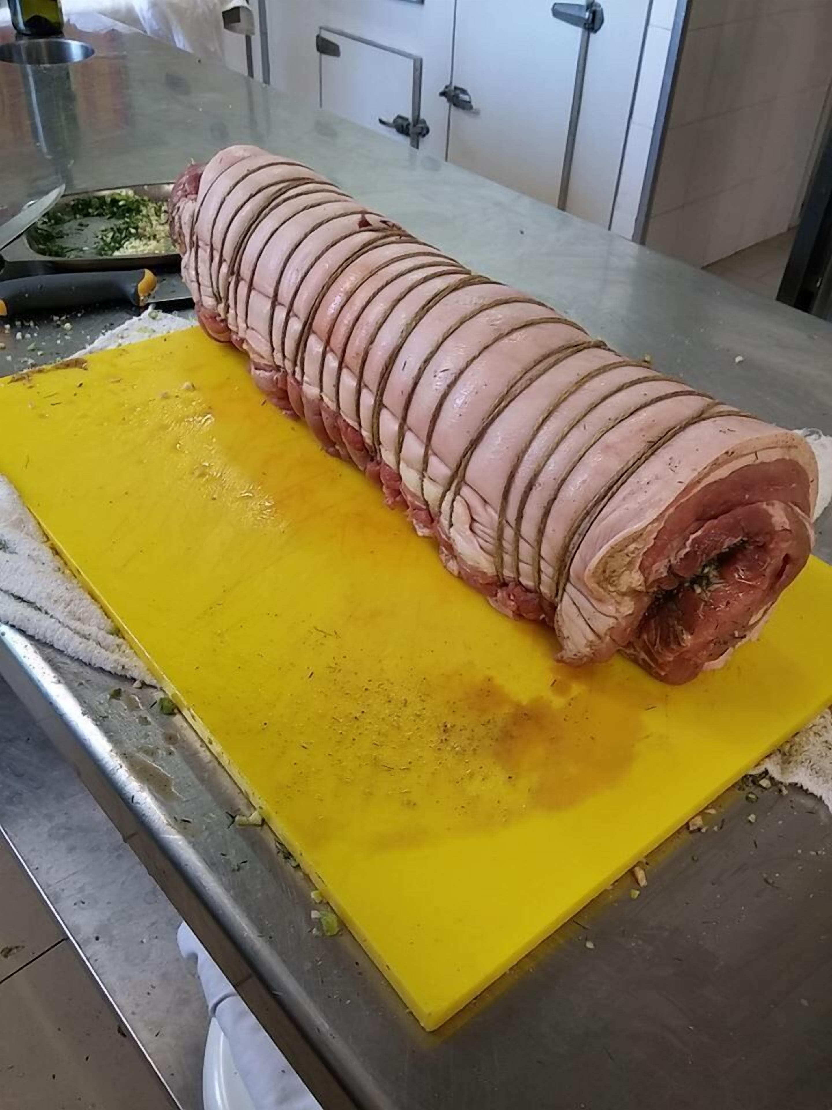 Un trozo grande de carne, cortado con precisión, sobre una tabla amarilla en una cocina.