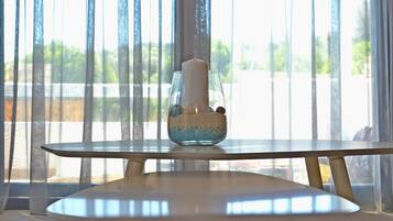 A table with a candle in a glass holder, a bowl with decorative items, and a view through sheer curtains.