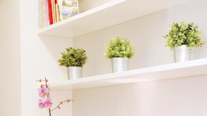 A room with a white shelf holding books, potted plants, and a decorative item. There are two cushioned stools in front. - Bye Bye Roma Pantheon Suite (Rome)