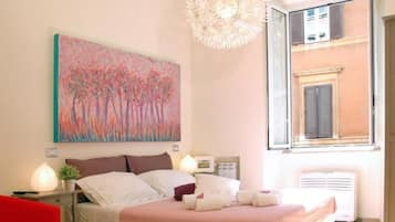 Ein Schlafzimmer mit einem Bett, Nachttischen, einem Gemälde, einem Fenster und Blick auf ein Gebäude.