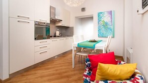 A modern kitchen with white cabinets, a built-in oven, and a dining area with a table and chairs. - Bye Bye Roma Pantheon Suite (Rome)