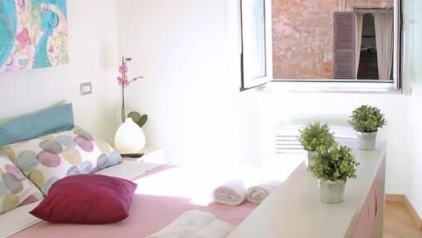 A bedroom with a bed, a bedside table, a window with a view of a building, and a hanging light fixture. - Bye Bye Roma Pantheon Suite (Rome)