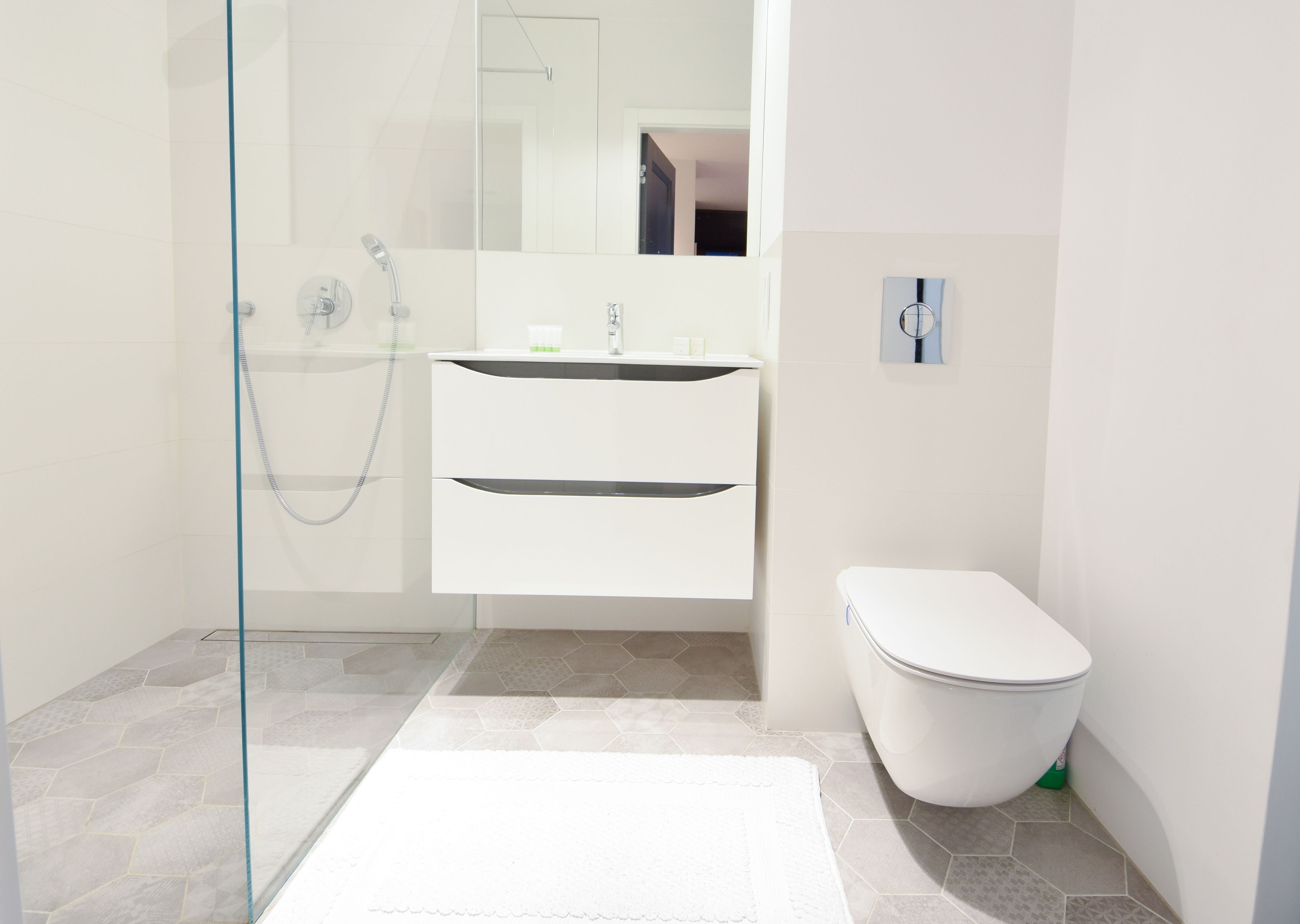 A modern bathroom with a glass shower enclosure, a white sink with two drawers, a toilet, and a large mirror.