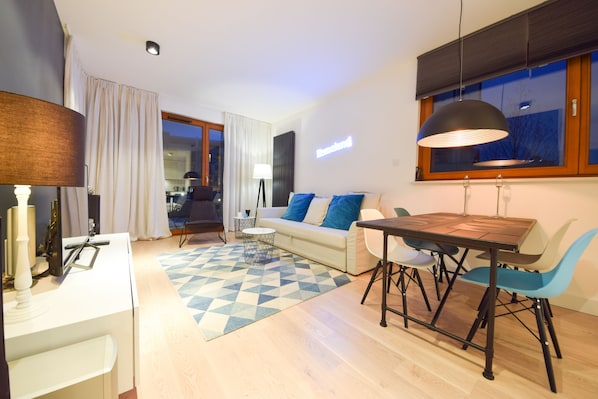 A modern living room with a dining area, a sofa with blue cushions, a wooden dining table, and a large window with a view.