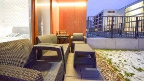 A modern outdoor seating area with wicker furniture and a view of a building with large windows. - ShortStayPoland Kieslowskiego - B41 (Warsaw)