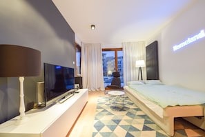 A hotel room with a bed, a TV, a lamp, a round table, and a view of the outside.