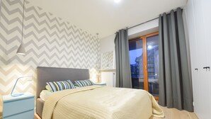 A bedroom with a bed, nightstand, and a view of the city at dusk. - ShortStayPoland Kieslowskiego - B41 (Warsaw)