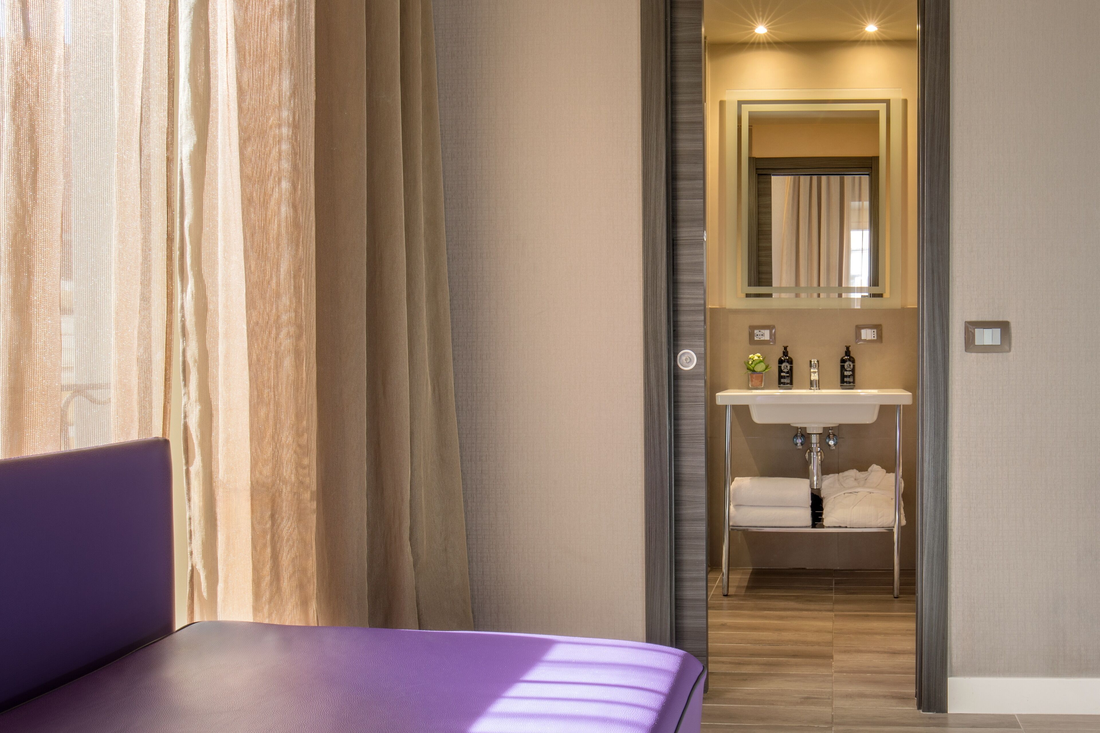 Habitación de hotel moderna con cama, baño con lavamanos y espejo.