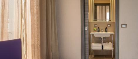 A modern hotel room with a bed, a bathroom with a sink, and a mirror.