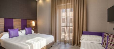 A hotel room with a large bed, a smaller bed, a TV, and a window with curtains.