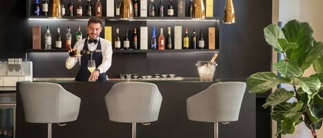 A bar area with a bartender, shelves of wine bottles, and bar stools.