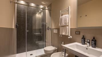 A modern bathroom with a glass-enclosed shower, a toilet, a bidet, and a sink with two bottles of soap.