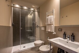 Un bagno moderno con doccia vetrata, un water, un bidet e un lavandino con due flaconi di sapone.