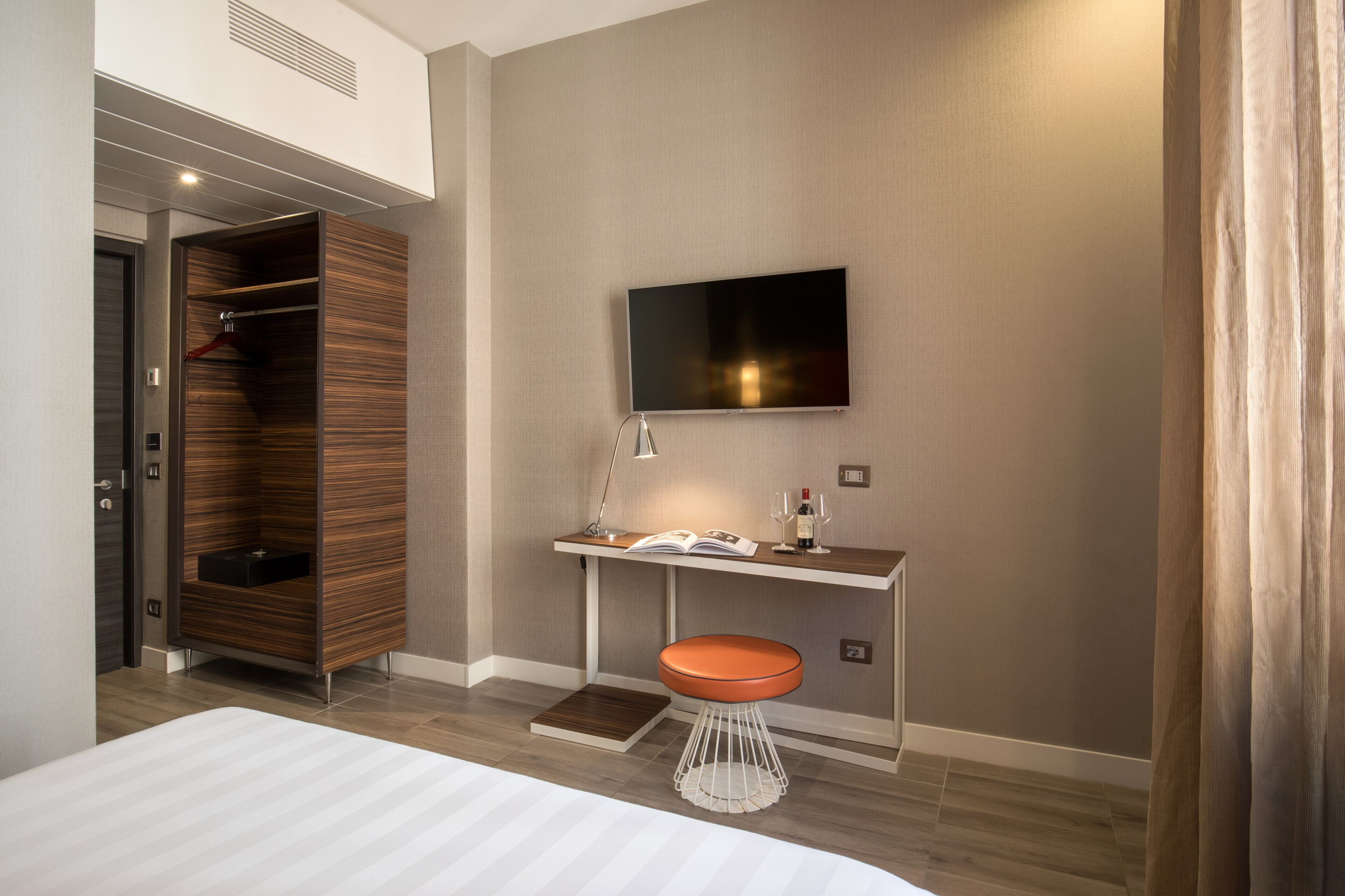 Quarto de hotel moderno com cama, escrivaninha com televisão, guarda-roupa e banheiro.