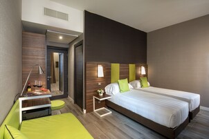 A modern hotel room with a large bed, a small desk, and a green sofa.