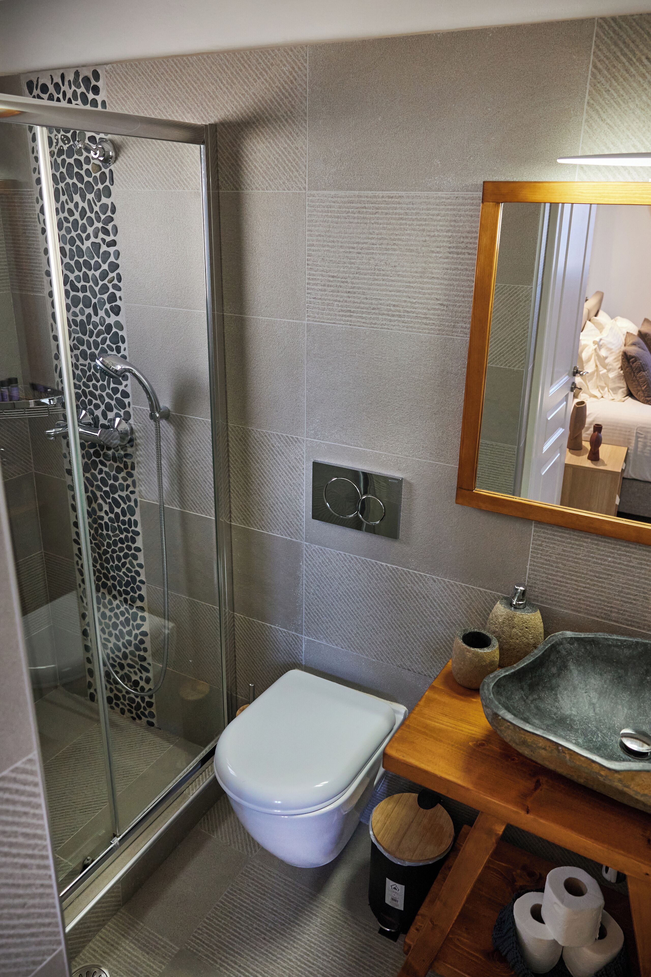 A modern bathroom with a glass-enclosed shower, a white toilet, and a wooden vanity with a large sink.