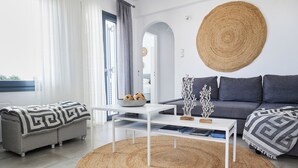 A modern living room with a white sofa, a white coffee table, a woven rug, and a grey couch with patterned throw blankets. - Sand Lily Mykonos (Mykonos)